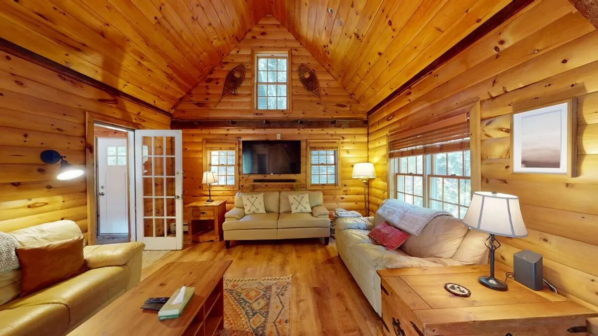 A warm living space with wooden walls, a comfortable sofa, a coffee table, a television, and soft lighting from lamps. The room exudes farmhouse charm and provides a setting for cozy evenings, game nights, or movie marathons.