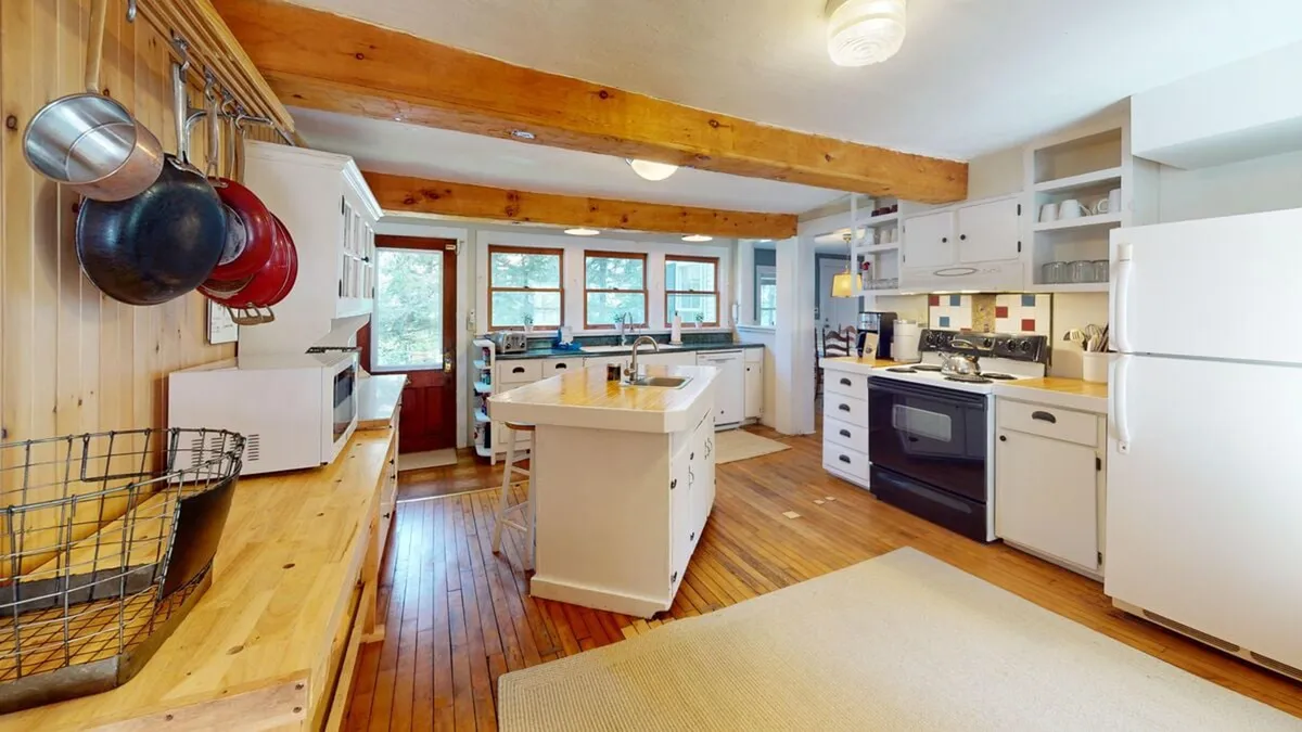 A spacious kitchen with a large central island, wooden beams overhead, stainless steel appliances, and windows that let in plenty of natural light. The scene is set for meal preparation, cooking, and socializing, with a welcoming and cozy atmosphere.