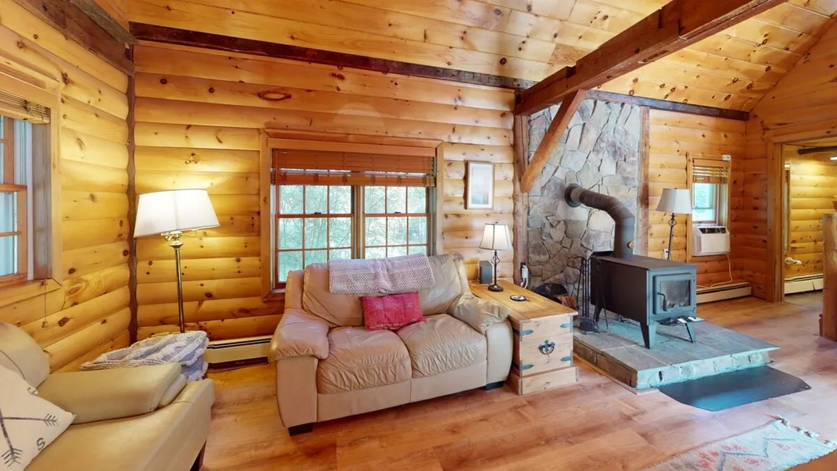 A living area with wooden beams, a stone fireplace, comfortable seating, and large windows letting in plenty of natural light. The room is ideal for sipping a hot drink by the fire, enjoying game nights, or simply unwinding while admiring the view.