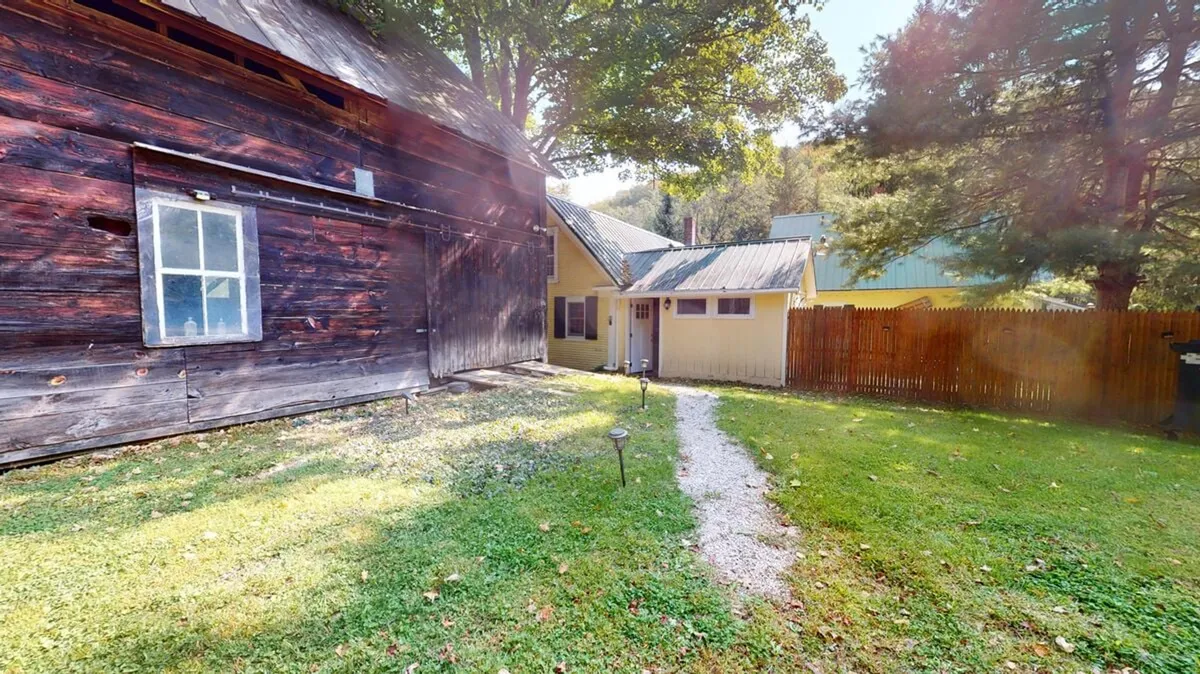 A charming scene with the rustic barn, yellow house, and a garden path winding through the yard. The setting is nostalgic and peaceful, ideal for sunset picnics, stargazing, and relaxed afternoons outside.