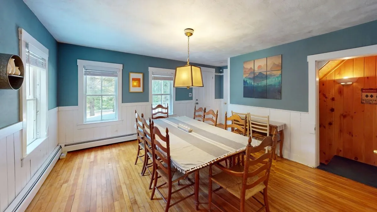 A long dining table with a striking hanging light fixture above and art on the wall, set in a welcoming and festive room. The scene suggests readiness for large gatherings, festive feasts, and memorable conversations.