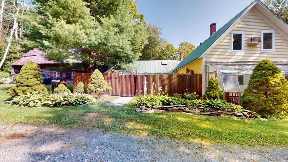 A view of flourishing flower beds, a wooden fence, a stone wall, and the farmhouse with a green roof; the garden setting is quiet and picturesque, suggesting opportunities for relaxation and mindfulness in a natural setting.