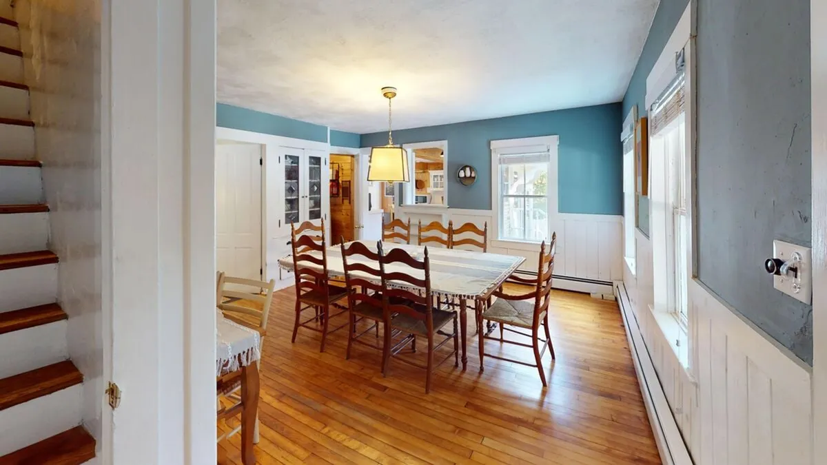 A bright dining area with a generous table, elegant light fixture, and wooden staircase in the background. The space is set for family meals, gatherings, and celebrations, with a warm and welcoming atmosphere.