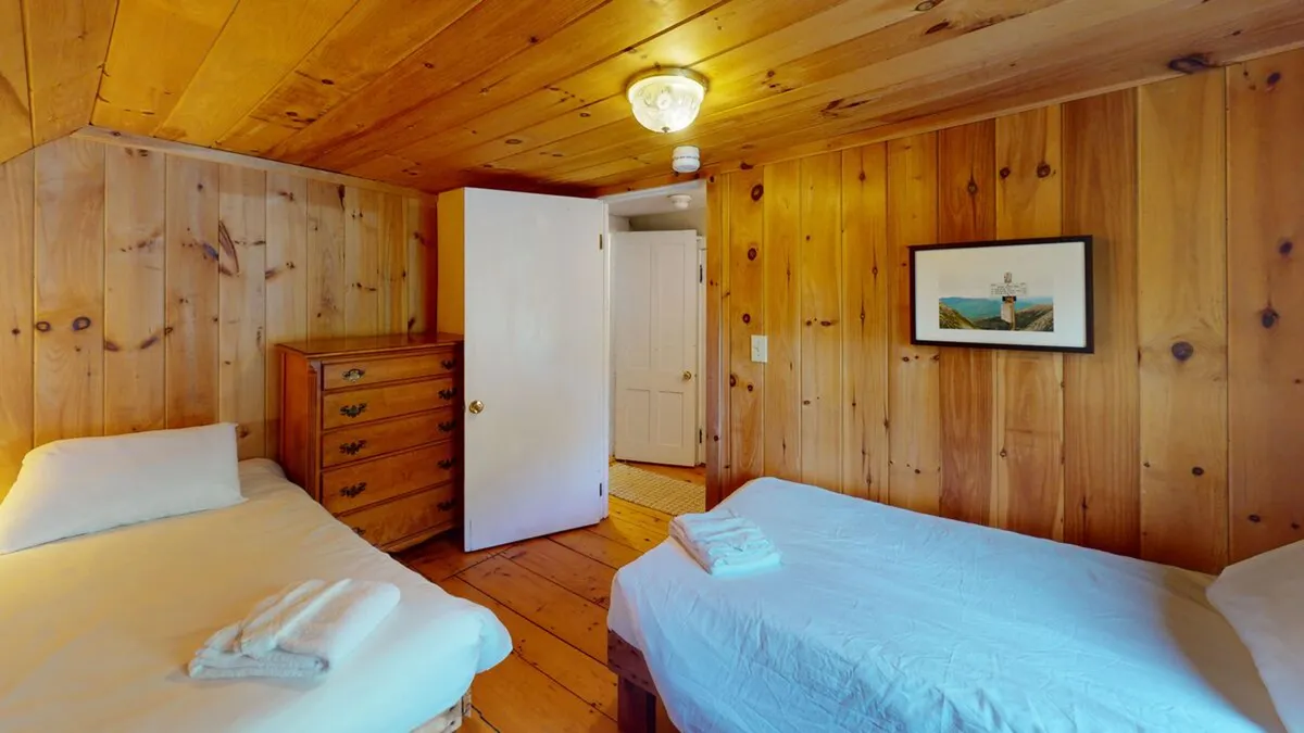 A warmly lit bedroom with two beds separated by a wooden dresser, framed artwork above, and soft bedding, providing an inviting atmosphere for families or friends sharing the space. The room feels both private and welcoming.